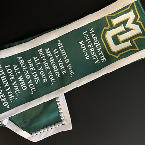 May include: Green and white graduation sash with the Marquette University logo and the text "Bound" and "Behind you, all your memories. Before you, all your dreams. Around you, all who love you. Within you, need."