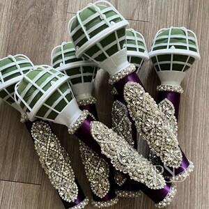 Peut inclure: Cinq porte-bouquets floraux violets et blancs avec des embellissements en strass. Les porte-bouquets sont en mousse et ont une cage en fil de fer vert.