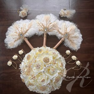 May include: A bridal bouquet with white roses, pearls, and gold accents. The bouquet is surrounded by three white feather fans with gold accents and four smaller white rose boutonnieres with gold accents. The text "Royalty Studio Designs" is visible in the bottom right corner of the image.
