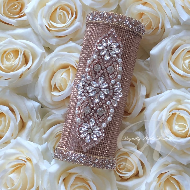 May include: A rose gold beaded clutch with a crystal and pearl design. The clutch is surrounded by white roses.
