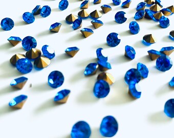 Può includere: Una spolverata di strass blu con montature dorate su uno sfondo bianco.