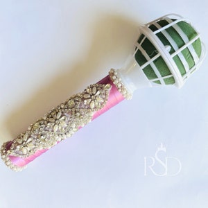 Peut inclure: Un porte-bouquet floral rose et blanc avec une garniture d&eacute;corative en strass. Le porte-bouquet est en mousse et a une cage en fil de fer.