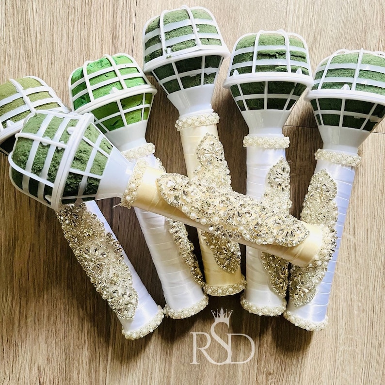 Peut inclure: Six supports de mousse florale blancs avec des inserts en mousse verte et une garniture de strass d&eacute;corative. Les supports sont envelopp&eacute;s de ruban de satin blanc.