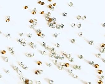 Puede incluir: Una dispersión de pequeños diamantes de imitación transparentes y dorados sobre una superficie blanca.