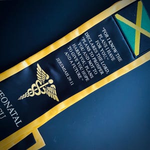 May include: Black and gold graduation sash with a medical symbol and the text "FOR I KNOW THE PLANS I HAVE FOR YOU," DECLARES THE LORD, "PLANS TO PROSPER YOU AND NOT TO HARM YOU, PLANS TO GIVE YOU HOPE AND A FUTURE." JEREMIAH 29:11"