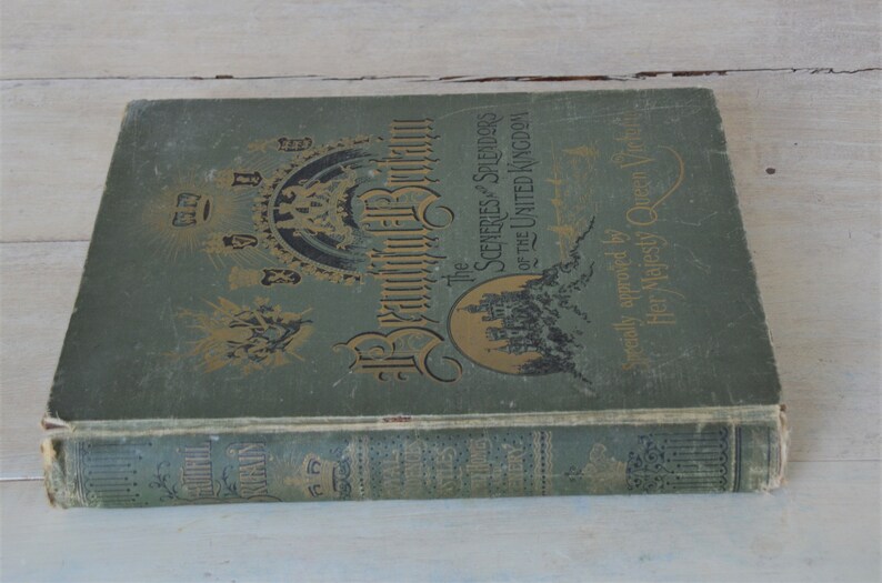 Op de afbeelding: Een groen hardback boek getiteld "The Sceneries & Splendors of the United Kingdom" met gouden letters en illustraties. Het boek is speciaal goedgekeurd door Hare Majesteit Koningin Victoria.