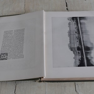 Op de afbeelding: Een open boek met een zwart-witfoto van een stadsgezicht en een rivier. De linkerpagina bevat tekst en een kleine zwart-witte illustratie.