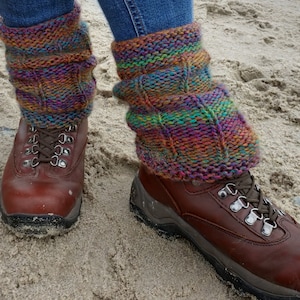 Könnte beinhalten: Ein Paar braune Lederstiefel mit bunten Strickgamaschen. Die Stiefel haben Schnürsenkel und werden auf sandigem Untergrund getragen.