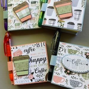 May include: Four different coffee themed notepad sets with pens attached. Each notepad has a different design with coffee cups and the words "coffee", "Rise", "Bio", and "happy".