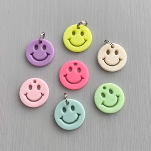 May include: Seven colorful smiley face charms with silver jump rings. The charms are in shades of pink, yellow, green, and blue.