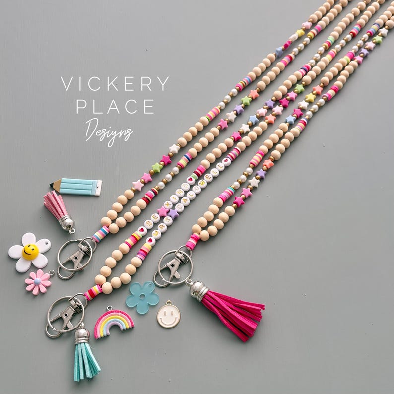 May include: Wooden bead lanyards with colorful accents and charms. The lanyards feature wooden beads, star-shaped beads, and letter beads spelling out words. Charms include a pencil, flowers, a rainbow, and a smiley face.