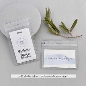 May include: Clear plastic badge holders with a white card inside. The card features the text "Vickery Place Designs" in black. A sprig of green leaves rests nearby. The text "Text" is printed on the top left of the badge holder.