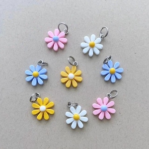 May include: A collection of eight daisy-shaped charms, each featuring a metal jump ring. The charms come in various colors, including pink, white, yellow, and light blue, with contrasting centers in yellow, white, or light blue.