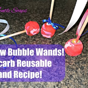 May include: Three red bubble wands with white and blue ribbon streamers attached to wooden sticks. The wands are made from a reusable material and are labelled "New Bubble Wands! Bicarb Reusable Wand Recipe!"