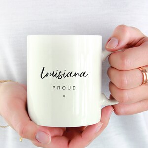 May include: White ceramic mug with black text that reads "Louisiana Proud" with a small "x" below the text.