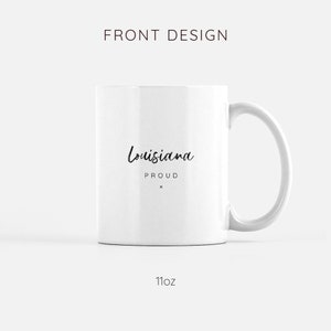 May include: White ceramic mug with a black handwritten design that says "Louisiana Proud" on the front. The mug is 11 ounces.