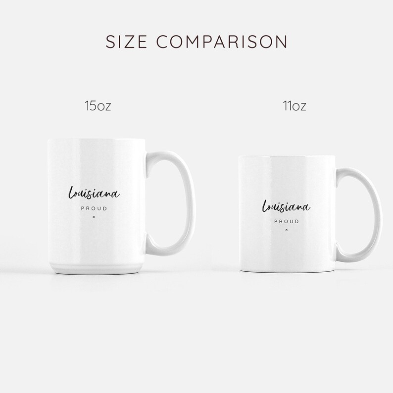 May include: Size comparison of two white ceramic mugs. The larger mug is 15 oz and the smaller mug is 11 oz. Both mugs feature black text that reads "Louisiana Proud".