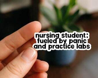 May include: A white sticker with black text that reads "nursing student: fueled by panic and practice labs." The sticker is held by a hand, with a blurred background of a plant in a dark blue pot.