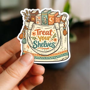 Op de afbeelding: Een sticker met een cr&egrave;mekleurige draagtas gevuld met boeken, een rol en bladeren. De tas heeft de tekst "Treat Your Shelves" in oranje en groen. De boeken hebben decoratieve covers met bloemen- en hemelse ontwerpen.