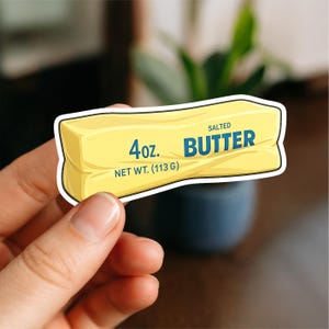 May include: A rectangular sticker shaped like a stick of yellow butter with a white border. The text on the sticker reads 4oz. SALTED BUTTER NET WT. (113 G) in blue lettering. The design features a stylised illustration of a butter stick.