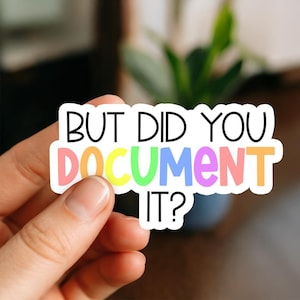 May include: A white sticker with the text "BUT DID YOU DOCUMENT IT?" in black and colourful letters. The word "DOCUMENT" is in rainbow colours. The sticker is held by a hand.