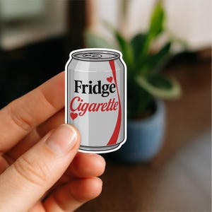 May include: A sticker depicting a silver can with the words "Fridge Cigarette" in black and red, and red heart accents. A red curved stripe runs down the side. The sticker is held by a hand.