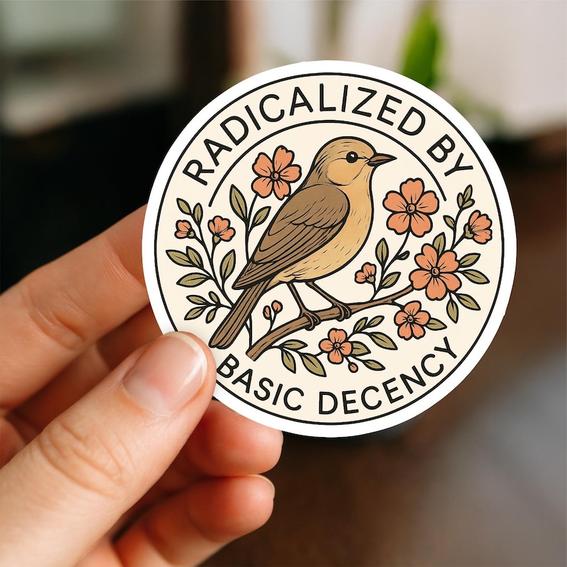 May include: A round sticker with the text "RADICALIZED BY BASIC DECENCY" encircling a bird perched on a flowering branch. The bird is brown and tan, the flowers are peach, and the background is cream.