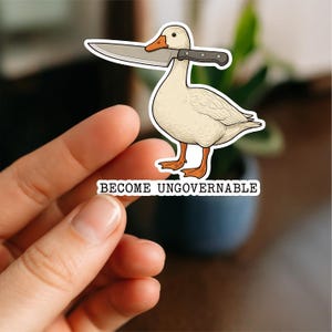 May include: A sticker depicting a cartoon duck with a knife through its neck. The duck is white with orange feet and beak. The text "BECOME UNGOVERNABLE" is printed below the duck.