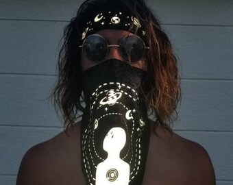 Pode incluir: Um bandana preto com um desenho branco de uma pessoa cercada por planetas e estrelas. O bandana está amarrado em torno da cabeça de uma pessoa que usa óculos de sol.