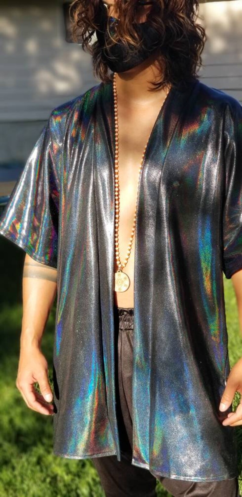 May include: A black iridescent kimono with a gold chain necklace and a circular pendant. The kimono has a V-neck and long sleeves.