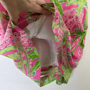 May include: A pink and green patterned dress with a white lining. The dress features a tropical print with palm leaves and floral designs. The edges of the dress have a decorative cut-out design.