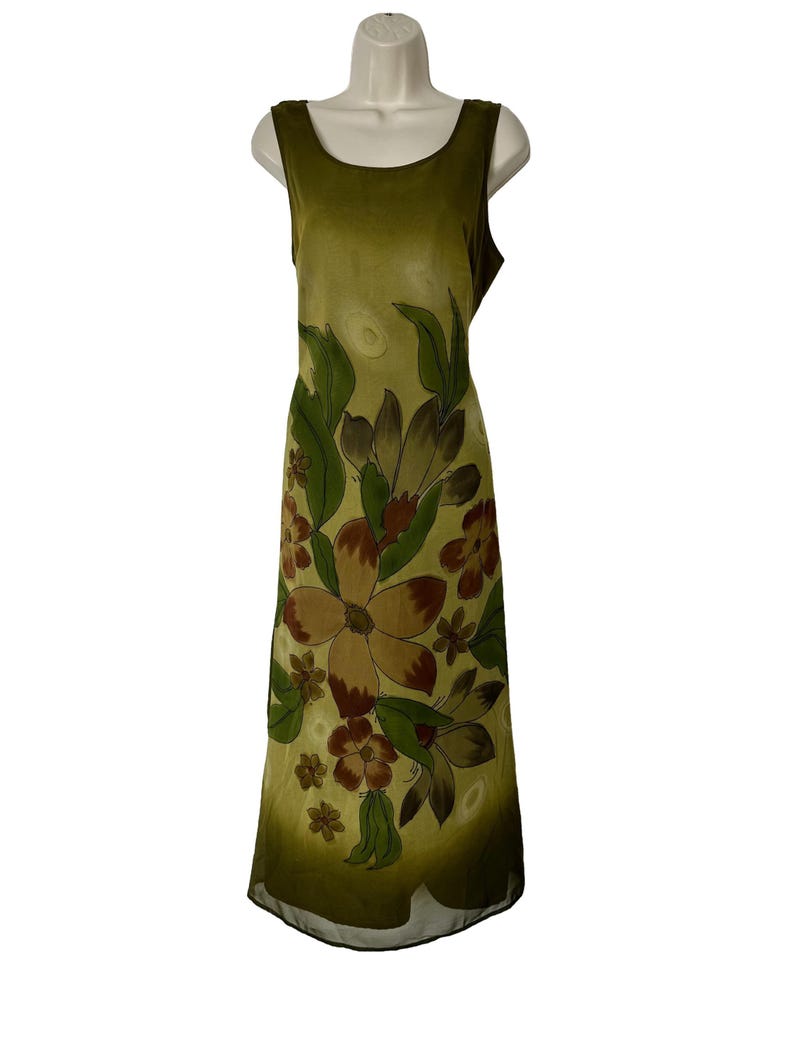 K&ouml;nnte beinhalten: Olivgr&uuml;nes &auml;rmelloses Kleid mit floralem Muster. Das Kleid hat gro&szlig;e braune und gr&uuml;ne Blumen mit gr&uuml;nen Bl&auml;ttern. Das Kleid wird auf einer wei&szlig;en Schaufensterpuppe pr&auml;sentiert.