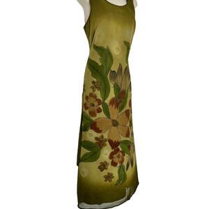 K&ouml;nnte beinhalten: Olivgr&uuml;nes &auml;rmelloses Kleid mit floralem Muster. Das Kleid hat gro&szlig;e braune und beige Blumen mit gr&uuml;nen Bl&auml;ttern. Das Kleid wird auf einer Schaufensterpuppe pr&auml;sentiert.