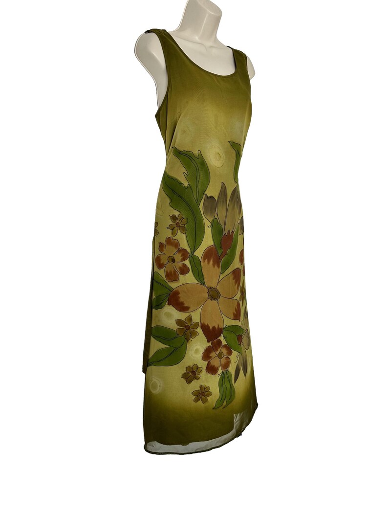 K&ouml;nnte beinhalten: Olivgr&uuml;nes &auml;rmelloses Kleid mit floralem Muster. Das Kleid hat gro&szlig;e braune und beige Blumen mit gr&uuml;nen Bl&auml;ttern. Das Kleid wird auf einer Schaufensterpuppe pr&auml;sentiert.