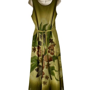 K&ouml;nnte beinhalten: Ein &auml;rmelloses, bodenlanges Kleid in Olivgr&uuml;n- und Gelbt&ouml;nen mit einem Blumenmuster in Braun und Gr&uuml;n. Das Kleid hat eine taillierte Taille mit passendem G&uuml;rtel.