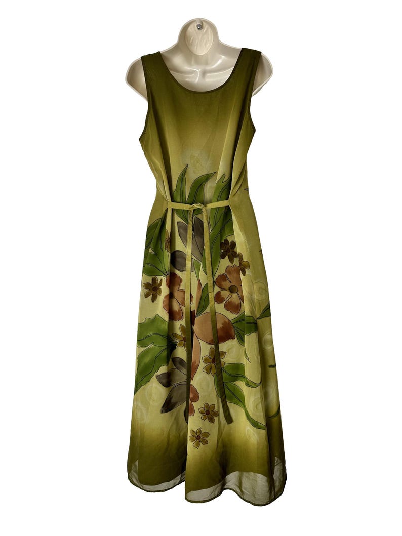 K&ouml;nnte beinhalten: Ein &auml;rmelloses, bodenlanges Kleid in Olivgr&uuml;n- und Gelbt&ouml;nen mit einem Blumenmuster in Braun und Gr&uuml;n. Das Kleid hat eine taillierte Taille mit passendem G&uuml;rtel.