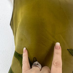 K&ouml;nnte beinhalten: Olivgr&uuml;nes &auml;rmelloses Kleid mit einem dunkelgr&uuml;nen Blumenmuster. Das Kleid besteht aus einem leichten, flie&szlig;enden Stoff. Es hat einen Rundhalsausschnitt und ein schlichtes, elegantes Design. Ein Sommerkleid.
