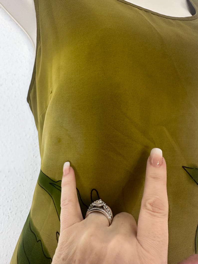 K&ouml;nnte beinhalten: Olivgr&uuml;nes &auml;rmelloses Kleid mit einem dunkelgr&uuml;nen Blumenmuster. Das Kleid besteht aus einem leichten, flie&szlig;enden Stoff. Es hat einen Rundhalsausschnitt und ein schlichtes, elegantes Design. Ein Sommerkleid.