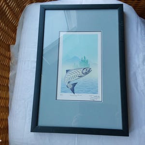 Peut inclure: Impression d'art encadrée représentant un saumon stylisé sautant hors de l'eau, avec en arrière-plan des montagnes et des arbres. L'œuvre utilise des nuances de bleu et de gris, avec le titre "Morning Mist" et la signature de l'artiste.