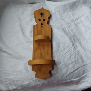 May include: A wooden wall shelf with two shelves. The shelf has a carved floral design at the top and a simple, rounded shape at the bottom.