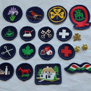 Könnte beinhalten: Eine Sammlung von 15 gestickten Abzeichen, meist blau mit weißen Nähten, mit verschiedenen Designs, darunter ein Ahornblatt, ein Haus, ein Kreuz, ein Schlüssel, eine Nähmaschine, eine Tasse, ein Vogel, ein Kleeblatt, ein Mädchenführer-Logo und eine Schere.