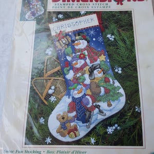 May include: A cross-stitch Christmas stocking kit with a festive snowman design. The stocking features snowmen in winter attire, with the name "CHRISTOPHER" at the top. The kit includes the words "STAMPED CROSS STITCH" and "POINT DE CROIX ESTAMPE".