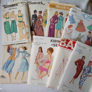 Op de afbeelding: Een verzameling vintage naaipatronen met illustraties van badkleding, jurken en andere kledingstukken. Merken zijn onder meer Butterick, Simplicity en Kwik Sew. De patronen zijn in verschillende maten en stijlen.