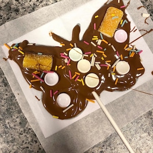 以下が含まれることがあります： 棒に刺さったチョコレートの蝶。スプリンクル、白いチョコレートキャンディー、黄色のグミキャンディーで飾られています。