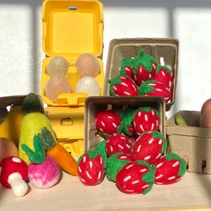 May include: A set of felt food items in various colors, including red strawberries, yellow pears, green carrots, and a peach. The felt food items are arranged in cardboard boxes.