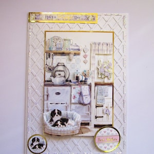 May include: A white card with a gold border and a white and gold lattice pattern. The card features a picture of a kitchen with a white stove, a teapot, and two dogs sleeping in a basket. The text "Have a Delightful Day" is on the top of the card and "Best Wishes" is on the bottom of the card.