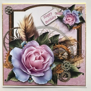 Könnte beinhalten: Eine handgemachte Grußkarte mit einer rosa und violetten Rose, goldenen Zahnrädern und Federn. Die Karte hat einen rosa Hintergrund und einen goldenen Rand. Der Text "Happy Birthday" ist auf einem weißen Etikett geschrieben.