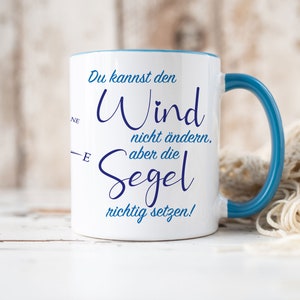 Può includere: Tazza in ceramica bianca con bordo e manico blu. La tazza ha una citazione in tedesco che recita "Du kannst den Wind nicht ändern, aber die Segel richtig setzen!" che si traduce in "Non puoi cambiare il vento, ma puoi regolare le vele correttamente!"