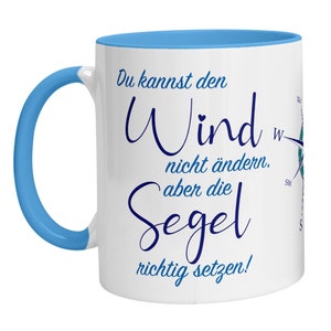 Può includere: Tazza in ceramica bianca con bordo e manico di colore blu chiaro. La tazza presenta una rosa dei venti e il testo "Du kannst den Wind nicht ändern, aber die Segel richtig setzen!" in blu.