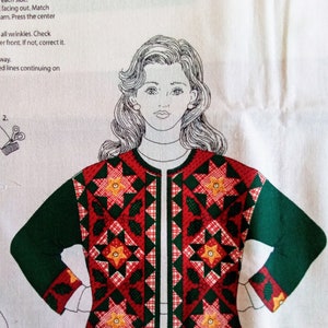 May include: A green and red cardigan with a quilted pattern featuring stars and holly leaves. The cardigan has a front zipper closure and long sleeves.